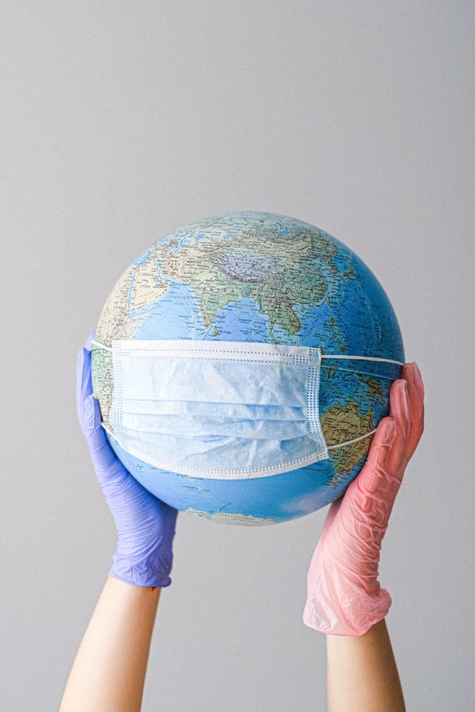 corona hands with latex gloves holding a globe with a face mask