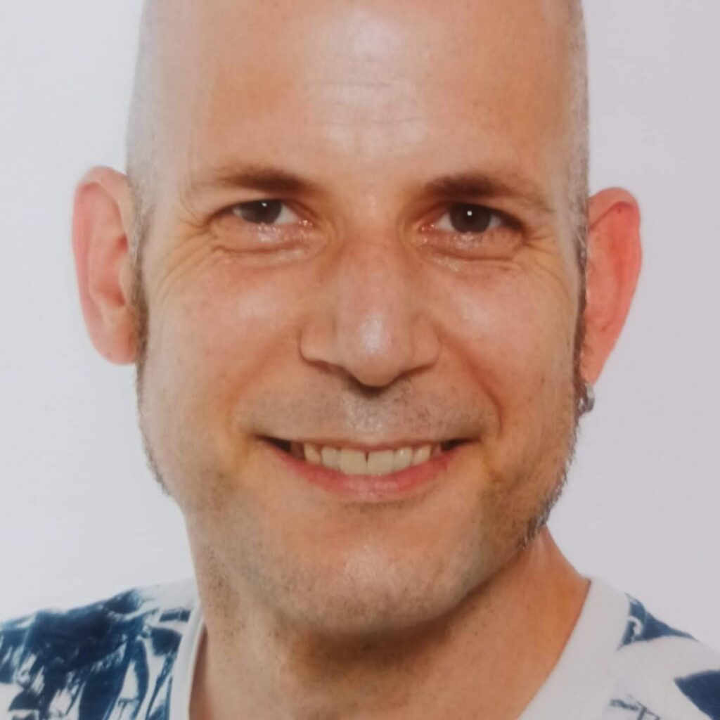 Stefan Jäkel lächelt in einem blau-weiß gemusterten Oberteil.