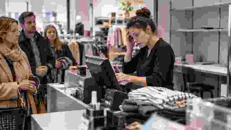 Verkäuferin arbeitet an einer Kasse, während Kunden warten und weitere Arbeitsplätze unbesetzt bleiben